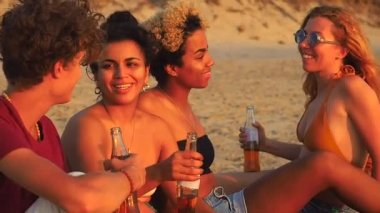 Afro-Amerikan, Hint ve Kafkas grubu gün batımında sahilde limonata içiyor.