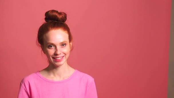 Rödhårig ingefära kvinna i rosa studio bakgrund, hennes bulle föll isär under skakning huvud — Stockvideo