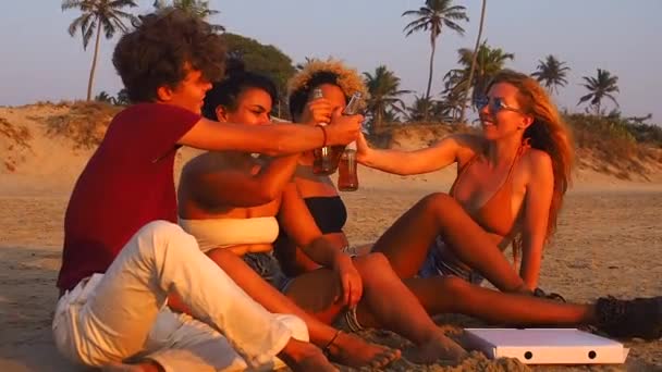 Afro-Amerikan, Hintli ve Kafkas grubu limonata içip şişeleri tokuşturarak gün batımında sahilde şerefe diliyor. — Stok video