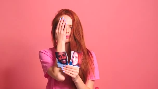 Pelirroja pelirroja mujer en rosa estudio de fondo rasgando tarjeta de fotos de sonriente pareja internacional — Vídeo de stock