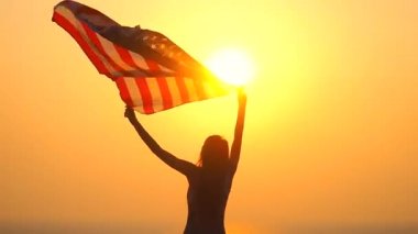Güneşin doğuşunda Amerikan bayrağıyla denizde güzel genç bir kadın.