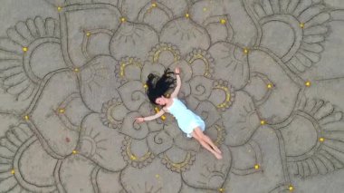 Kadın kumsalda büyük mandala çiziyor ve boş kumsalda dans ediyor. Dron kuadrokopterinin yukarısında. Kadınlık ve bağımsızlık kavramı.