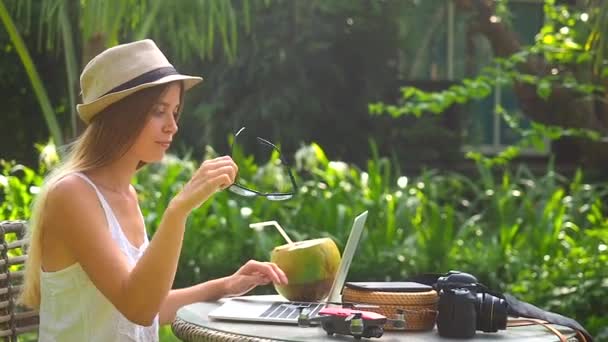 Femme blonde portant un chapeau de paille et travaillant dans un endroit tropical et boivent de la noix de coco — Video