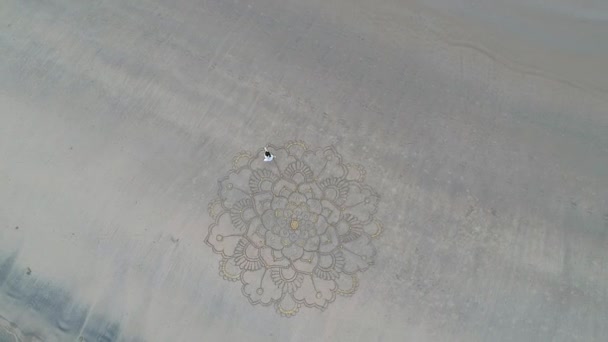 Woman drawing the big mandala at sand and dancing in empty beach top view above from drone quadrocopter.concept of femininity and independence — Stock Video