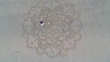 Kadın kumsalda büyük mandala çiziyor ve boş kumsalda dans ediyor. Dron kuadrokopterinin yukarısında. Kadınlık ve bağımsızlık kavramı.
