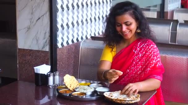 Mooie vrouw eten dosa chutney naan en indiaanse tali in een restaurant.Ze draagt rode sari met gouden oorbellen, met tilaka op haar voorhoofd — Stockvideo