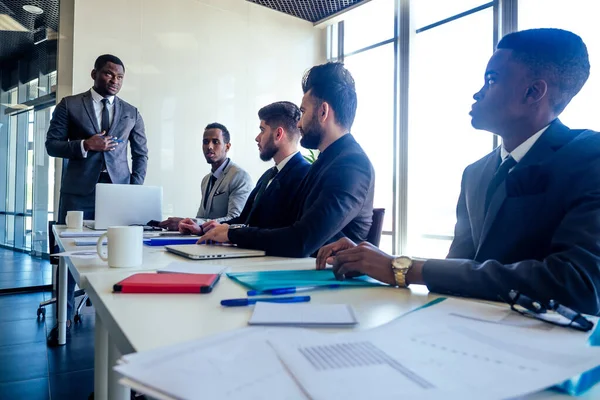 Boss afro businessmen talking with arab partners colleague, multiethnic team in the office with panorama window. — Stock Photo, Image