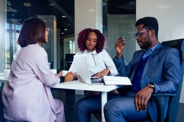 Çok kültürlü adamlardan oluşan yaratıcı bir ekip masanın etrafında resmi giysiler içinde oturmuş toplantı odasında yeni projeler hakkında konuşuyorlar.