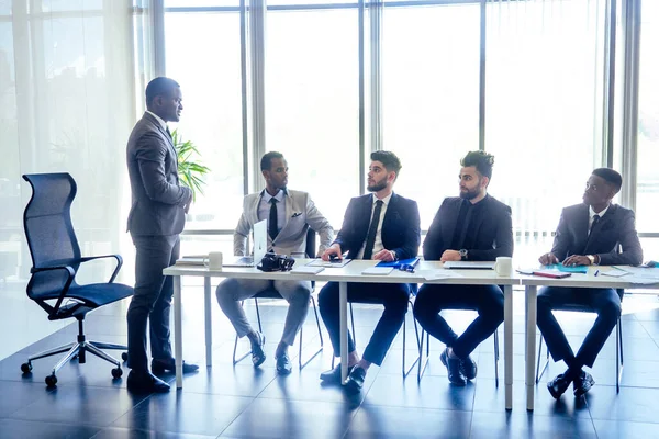 Boss afro businessmen talking with arab partners colleague, multiethnic team in the office with panorama window. — Stock Photo, Image