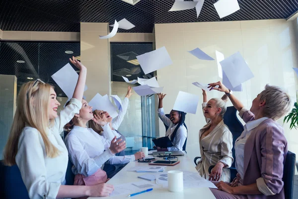 Multiracial grupp unga kvinnor redaktör för berömda tidningen samarbetar kasta papper upp dokument i öppna utrymme kontor i ett modernt kontor med panoramafönster — Stockfoto