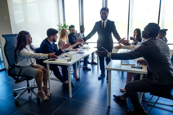 Creative team of multiracial men sitting round the desk in formal clothes talking over new project in meeting room — Stock Photo, Image