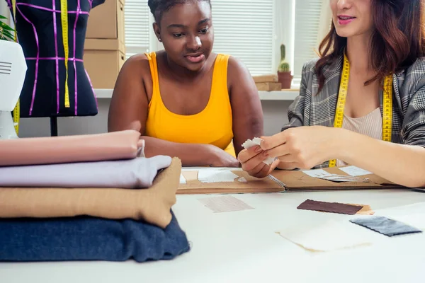 Hermosa costurera mujer con el pelo largo y cliente afro. sastre crea una imagen para ella en el taller de costura de la casa de moda —  Fotos de Stock