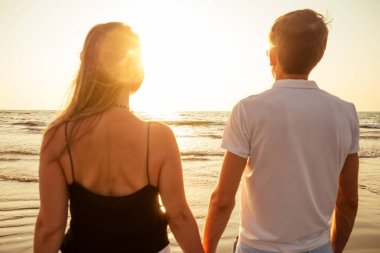 Tatil çifti gün batımında birlikte kumsalda yürüyor.