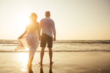 Tatil çifti gün batımında birlikte kumsalda yürüyor.