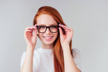 Kızıl saçlı kızıl kadın mutlu, gri stüdyo arka planında beyaz pamuklu tişört giyiyor.