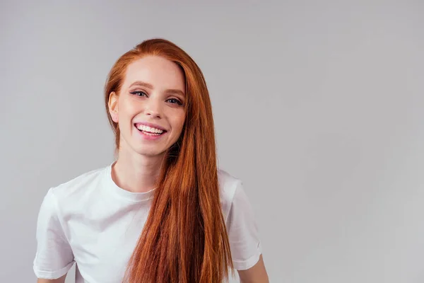 Rödhårig ingefära kvinna känner sig lycklig, bär vit bomull t-shirt i grå studio bakgrund — Stockfoto