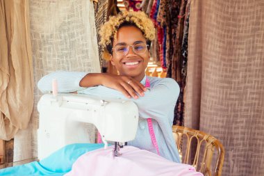 Afrika kökenli Amerikalı kadın Bali 'deki tropikal atölyesinde dikiş makinesinin yanında durup kollarını kavuşturdu.
