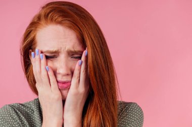 Kızıl saçlı mutsuz kadın yanağına dokunuyor, manikür yaptırıyor pembe stüdyo arka planında.