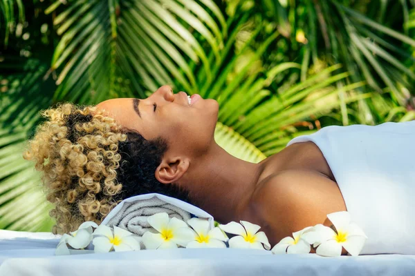 Vacker brasiliansk leende flicka ligger på bordet med handduk och vita blommor, massera och skämma bort sig själv i lyx resort spa i Bali — Stockfoto