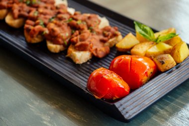 Lezzetli kırmızı fasulye ekmeğin üzerinde patates ve domates dikdörtgen siyah tabak organik vejetaryen yemeği.