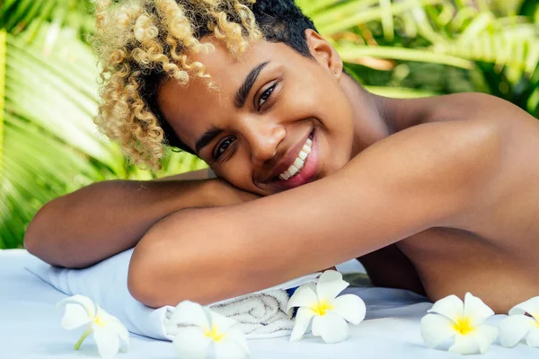 Prachtig Braziliaans lachend meisje liggend op tafel met handdoek en witte bloemen, masserend en verwennend in luxe resort spa centrum op Bali — Stockfoto