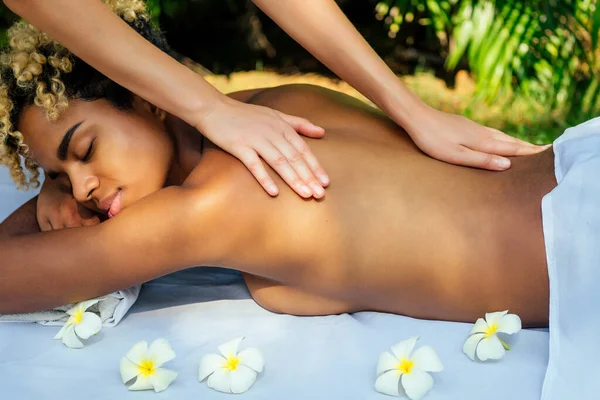 Hermosa chica brasileña sonriente tumbada en la mesa con toalla y flores blancas, masajeando y mimándose en el centro de spa de lujo resort en Bali — Foto de Stock