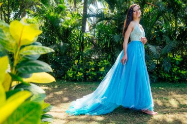 Hintli kadın yüzme havuzunun yanında mavi uzun elbiseli poz veriyor.