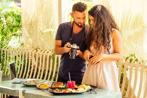 Красива індійська жінка і арабський чоловік фотографує посуд в літньому тропічному кафе на камеру — стокове фото