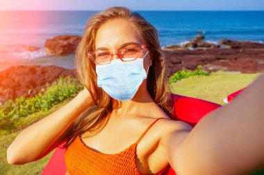 Güzel turuncu bir mercan mayo giymiş mutlu bir kız tatilde telefonda selfie çekiyor. Bikinili kadın elinde cep telefonu fotoğraf makinesi, akıllı telefon fotoğraf uygulaması okyanus Hindistan 'ında bir dinlenme yerinde oturuyor.