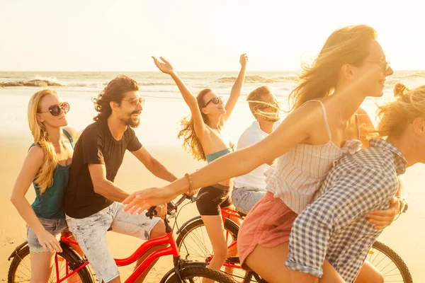 Joven grupo multiétnico de amigos divirtiéndose en la playa montando bicicletas cuando brote covid difusión está en el aire — Foto de Stock