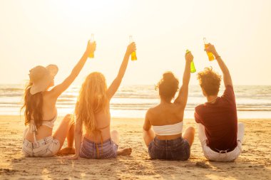 Mutlu uluslararası arkadaşlar sahildeki cam şişeden meyve suyu içiyor.