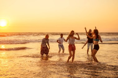 Çok kültürlü, çok uluslu mutlu insanlar güneşe karşı kaygısız ve mutlu bir şekilde koşuyorlar, denizde tatil yapıyorlar.