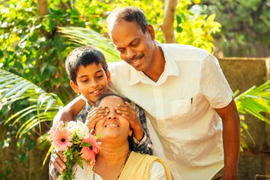 Hintli küçük çocuk elinde buket tutuyor ve dışarıda parkta annesine sürpriz yapıyor.