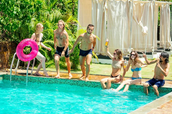 Group of happy six friends drinking jumping in pool day party with splash — Stock Photo, Image