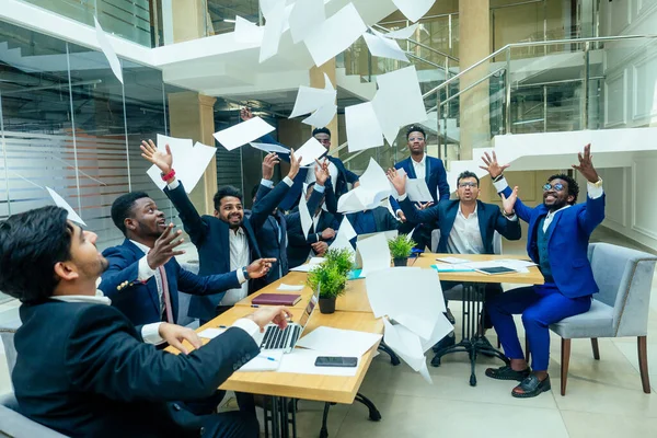 Internationell grupp av nio afrikanska amerikanska och indiska människor som har roligt och kasta upp papper efter hjärnstorm i stort kontor — Stockfoto