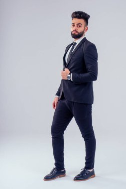 Stüdyoda şık takım elbiseli genç siyah saçlı adam beyaz arkaplanı izole ediyor.