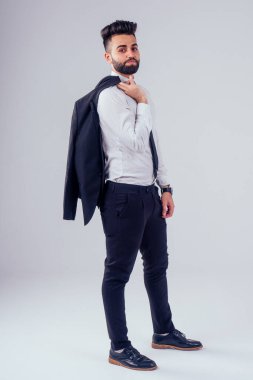 Stüdyoda şık takım elbiseli genç siyah saçlı adam beyaz arkaplanı izole ediyor.