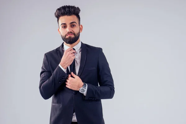 Joven turco guapo negro cabello hombre en elegante traje de negocios anudando la corbata en estudio aislar fondo blanco — Foto de Stock