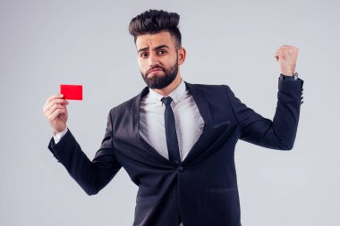 Stüdyoda kredi kartı tutan şık takım elbiseli Hintli genç, yakışıklı, siyah saçlı adam beyaz arka planı izole etti.