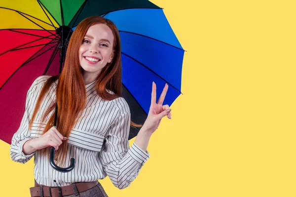 Schöne rothaarige Mädchen auf weißem Hintergrund im Stil gestreiftes Hemd mit Regenbogen einen Regenschirm. Herbst Mode Look saisonalen Frühjahrsverkauf — Stockfoto
