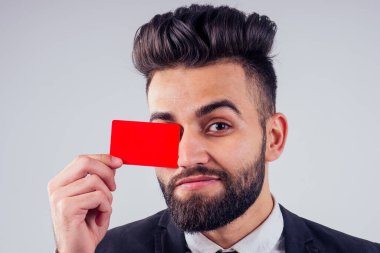 Stüdyoda kredi kartı tutan şık takım elbiseli Hintli genç, yakışıklı, siyah saçlı adam beyaz arka planı izole etti.