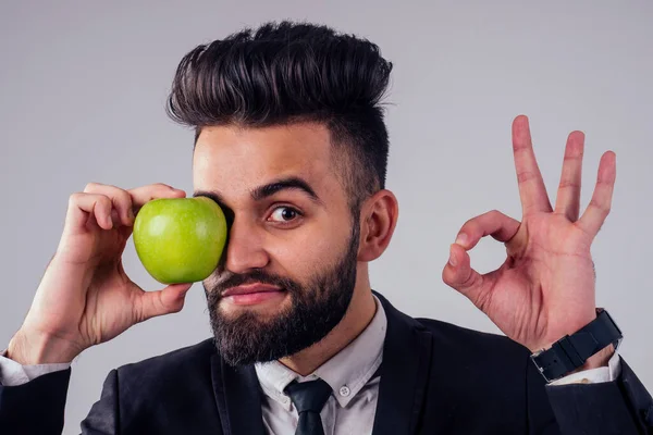 Joven guapo negro cabello hombre en elegante negocio traje comer verde manzana en estudio aislar blanco fondo — Foto de Stock