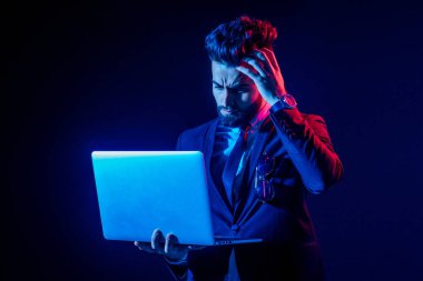 Türk yakışıklı siyah saçlı şık takım elbiseli adam üzgün dizüstü bilgisayara bakıyor çünkü stüdyodaki iflas etmiş salgın geçmişi soyutluyor