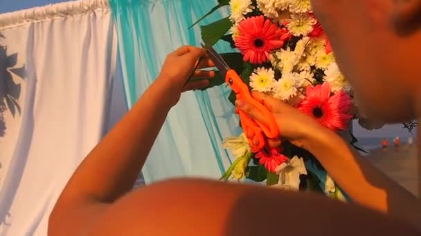 Decorador trabajando con la composición de flores para el arco de boda en la playa del océano — Vídeos de Stock
