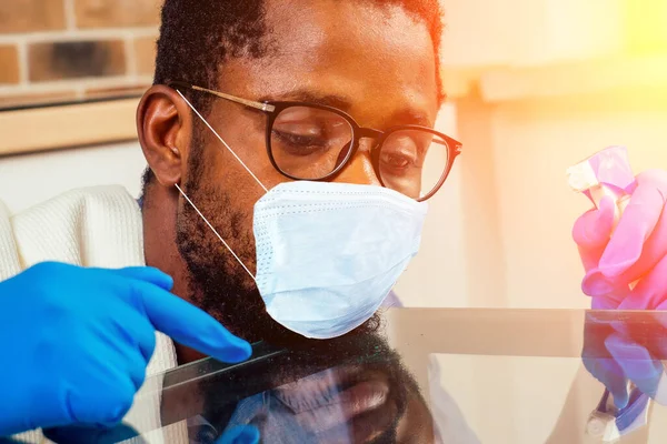 Homem africano em máscara médica limpeza fogão de cozinha capuz em casa, parede de tijolo fundo — Fotografia de Stock