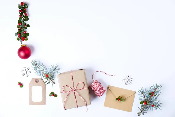 Weihnachtsrahmenkomposition. Weihnachtsgeschenk, Tannenzweig, rote Kugeln, Umschlag, weiße Holzschneeflocken, Schleife und rote Beeren. Draufsicht, flache Lage, Kopierraum. — Stockfoto