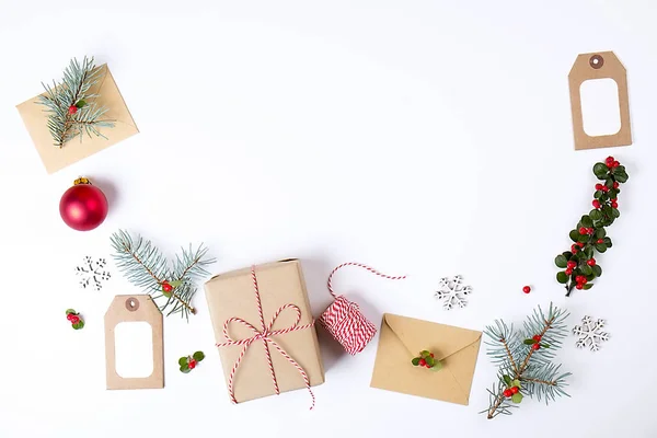 Weihnachtsrahmenkomposition. Weihnachtsgeschenk, Tannenzweig, rote Kugeln, Umschlag, weiße Holzschneeflocken, Schleife und rote Beeren. Draufsicht, flache Lage, Kopierraum. — Stockfoto