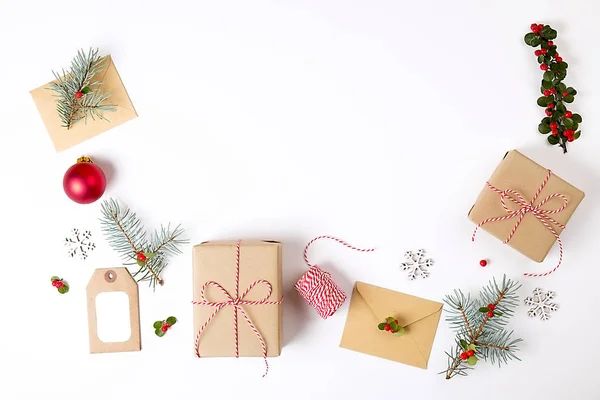 Weihnachtsrahmenkomposition. Weihnachtsgeschenk, Tannenzweig, rote Kugeln, Umschlag, weiße Holzschneeflocken, Schleife und rote Beeren. Draufsicht, flache Lage, Kopierraum. — Stockfoto