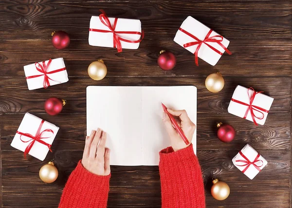 Γυναικείο χέρι γράφοντας ένα γράμμα προς Σάντα σε ξύλινα φόντο με χριστουγεννιάτικα δώρα — Φωτογραφία Αρχείου