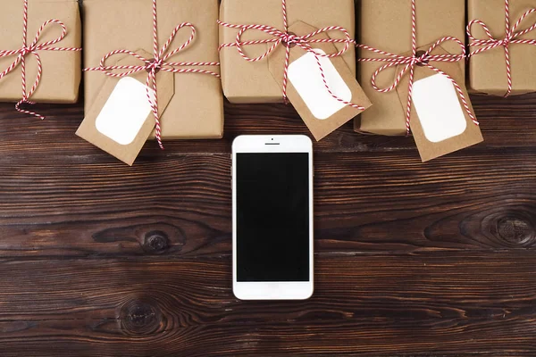 Smart phone with christmas presents on wooden background top view. Online holiday shopping concept. Flat lay, text space. Internet commerce on winter holidays concept.